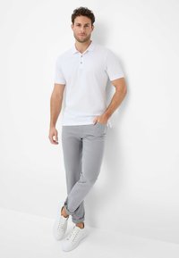 Weißes Poloshirt mit zwei Knöpfen, graue Slim-Fit-Hosen und weiße Sneakers. Glattes Material und klare Linien sorgen für einen minimalistischen Look.
