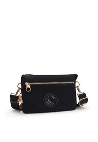Borsa a tracolla nera in nylon con zip dorata, patch con logo circolare, tracolla regolabile e dettaglio a charm. Texture liscia, forma rettangolare.