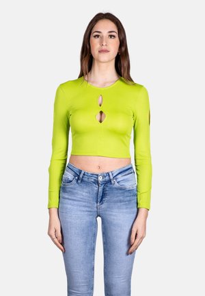 Top corto a maniche lunghe a coste verde lime con tre tagli a chiave; abbinato a jeans aderenti azzurri, vista frontale.