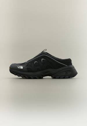 Musta slip-on-vaelluskenkä, jossa on kulutusta kestävä pohja, verkkokankaiset paneelit ja "The North Face" -logo varpaassa, neutraalia taustaa vasten.