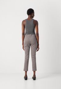 Graues Tanktop kombiniert mit gemusterten, knöchellangen Hosen in Schwarz-Weiß-Design; das Model trägt schwarze Schuhe und hat kurze Haare.