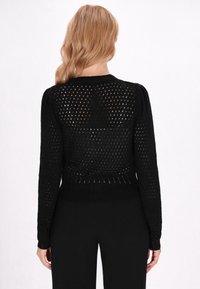 Maglione nero lavorato a maglia con un design a rete aperta, maniche lunghe, polsini a costine e vita aderente. Il retro è completamente scoperto con una leggera texture.
