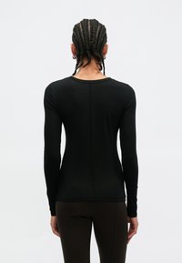 Top preto de manga comprida com decote redondo, design justo ao corpo e tecido texturizado. Apresenta costuras planas e costas lisas.