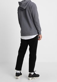 Grå huva sweatshirt med en avslappnad passform, ihop med svarta tapered byxor och svarta sneakers, som har vita detaljer och en vit undertröja.