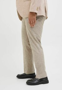 Pantalons en lin beige avec une coupe droite, associés à des chaussures noires à enfiler. Le tissu présente une texture subtile et une apparence légère.