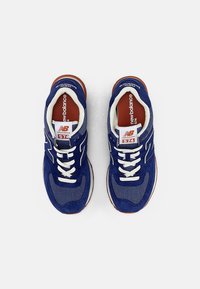 Blå mocka- och mesh-sneakers med vita snörningar och accenter, med en framträdande "N"-logotyp och vadderade bruna gummisulor.