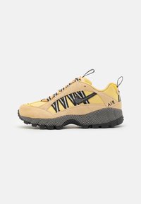 Gula och beige sneakers med svarta accenter, texturerat mockamaterial, zickzackmönster och slitstark sula, med draremmar på hälen.