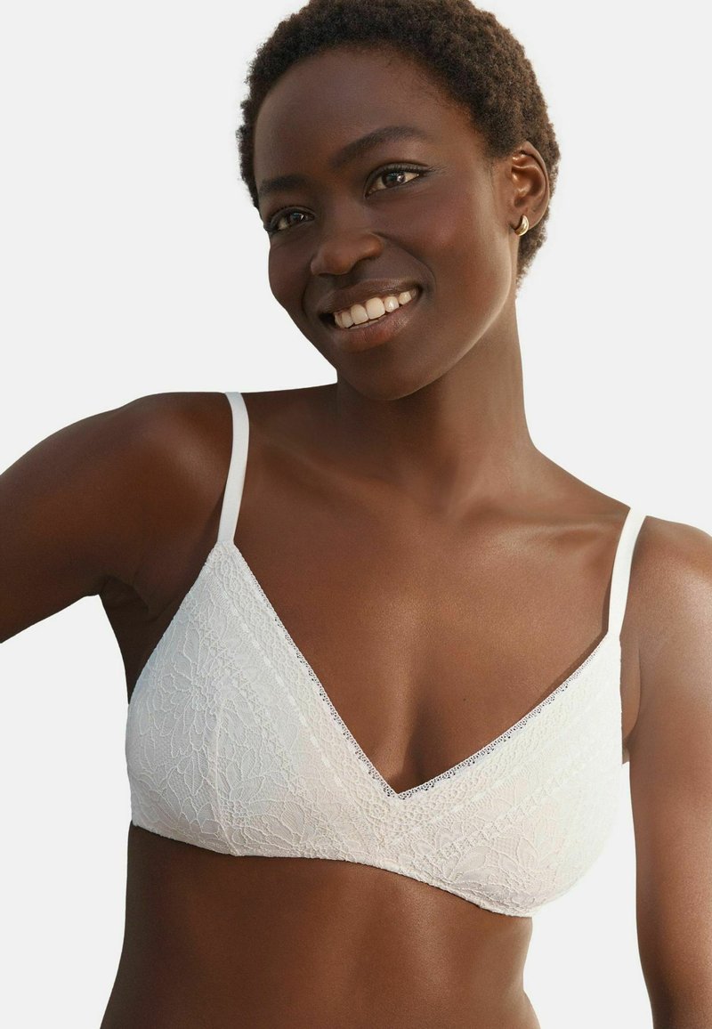 Valkoinen pitsinen bralette, jossa on kolmion muoto, säädettävät ohuet olkaimet, kukkakuosi ja V-muotoinen kaula-aukko. Pehmeä tekstuuri.