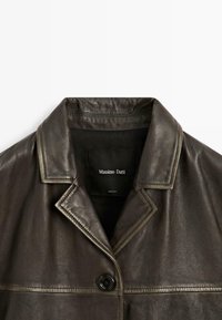 Tmavě hnědá kožená bunda s širokým límcem, jediným černým knoflíkem a viditelným šitím na hrudi a oblasti límce.