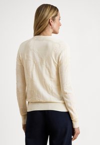 Svetlo béžový pletený sveter s textúrovaným vzorom, rebrovanými manžetami a lemom, s priliehavým strihom a okrúhlym výstrihom.