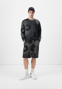 Schwarze und graue Sweatshirt und Shorts mit großen kreisförmigen Mustern. Aus strukturiertem Stoff, kombiniert mit weißen Sneakers und hellen Socken.