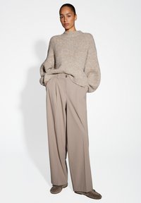 Beige chunky knit sweater with ribbed texture paired with light brown wide-leg trousers and soft brown slip-on shoes, against a white background.