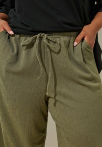 Pantalons en vert olive, texturés, avec taille élastique et cordon de serrage ajustable. Comprend des poches latérales et une coupe décontractée.