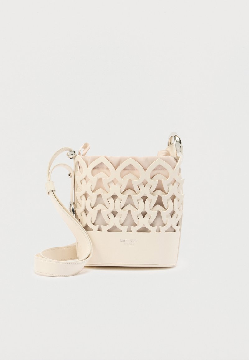 Τσαντάκι χιαστί από κρέμ δέρμα με γεωμετρικό σχέδιο κοπής, ρυθμιζόμενο λουράκι και απαλό υφασμάτινο επένδυμα στο εσωτερικό.