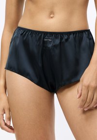 Fekete selyemcérna rövidnadrág, elasztikus derékpánttal, a elején egy kis fehér Calvin Klein logóval. Simaság és testhezálló fazon jellemzi.