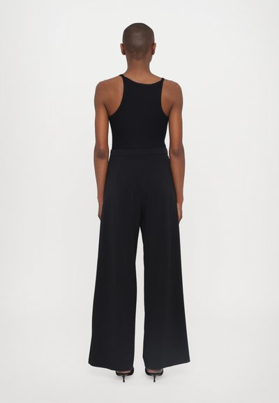 Melns top ar siksnām, apvienots ar plašām melnām biksēm. Apģērbs ir ar gludu tekstūru un pieguļošu jostu, bez redzamām rakstu vai akcentu detaļām.