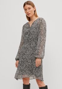Zwart-wit gevlekte midi-jurk met een V-hals, lange doorschijnende mouwen en een ontspannen pasvorm. Lichtgewicht, gestructureerde stof met een vloeiende silhouet.
