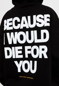 Sudadera negra con gran texto en blanco en la parte de atrás: "PORQUE MORIRÍA POR TI". Logotipo amarillo de "MULTIPLY APPAREL" en el borde inferior.