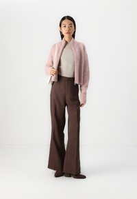 Cárdigan de felpa rosa claro con cierre, top beige acanalado y pantalones de pierna ancha marrones de cintura alta, complementados con botas de tacón marrones medianas.