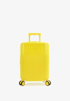 Valigia rigida gialla con quattro ruote girevoli e manico telescopico esteso, in piedi su sfondo bianco.