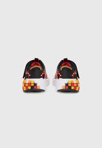 Black sneakers with a textured upper, featuring a patterned heel in red, yellow, and black, and a white, segmented sole. Accented with orange.