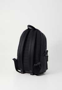 Mochila negra con un diseño texturizado y aerodinámico, correas ajustables y un asa superior, con un bolsillo lateral con cremallera para almacenamiento.
