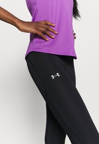 Lila tränings t-shirt i kombination med svarta leggings. Leggingsen har en silver Under Armour-logotyp, slät textur och en åtsittande design.