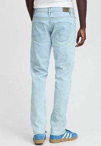 Jeans de mezclilla azul claro con pierna recta, cinturilla de altura media y dos bolsillos traseros con costuras angulares. Llevados con zapatillas deportivas azules.