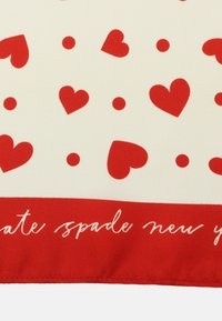 Czerwone serca i wzór kropek na kremowym tle z czerwonym obramowaniem, z napisem "kate spade new york" w białym kursywie.