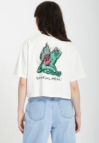 T-shirt blanc court avec un graphique coloré d'une grenouille entourée de flammes et d'un cœur, texte "RÉALITÉ SPIRITUELLE" en dessous, design simple, manches courtes.