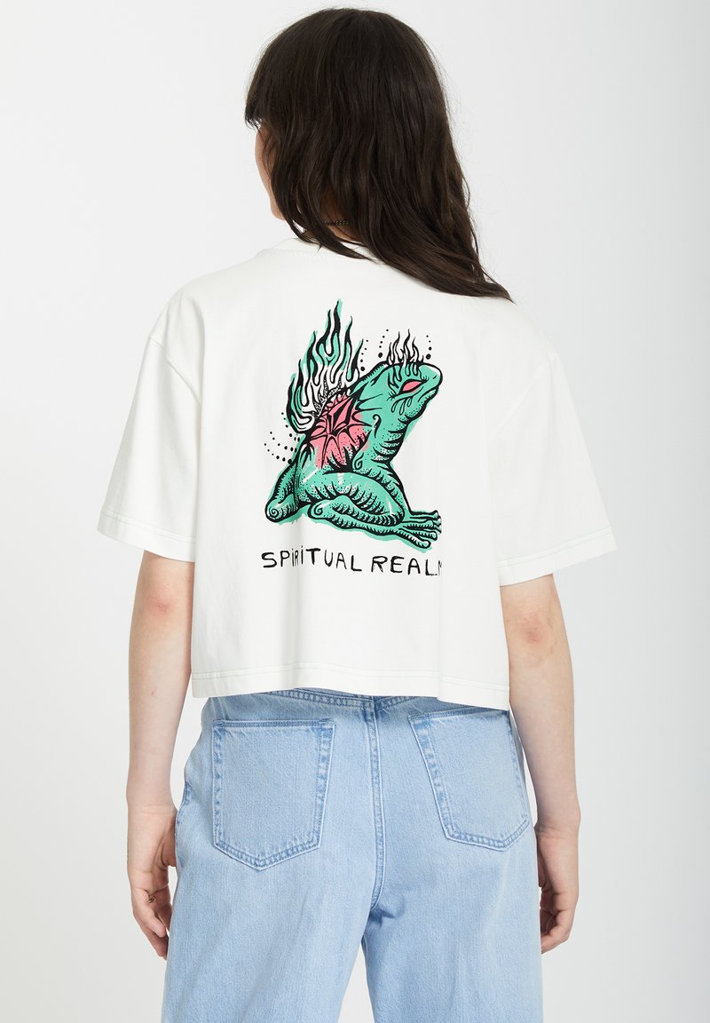T-shirt blanc court avec un graphique coloré d'une grenouille entourée de flammes et d'un cœur, texte "RÉALITÉ SPIRITUELLE" en dessous, design simple, manches courtes.