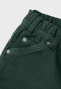 I pantaloni in corduroy verde scuro hanno una vita aderente, dettagli in metallo sui bottoni e una sottile texture a coste, che mette in mostra robuste cuciture.