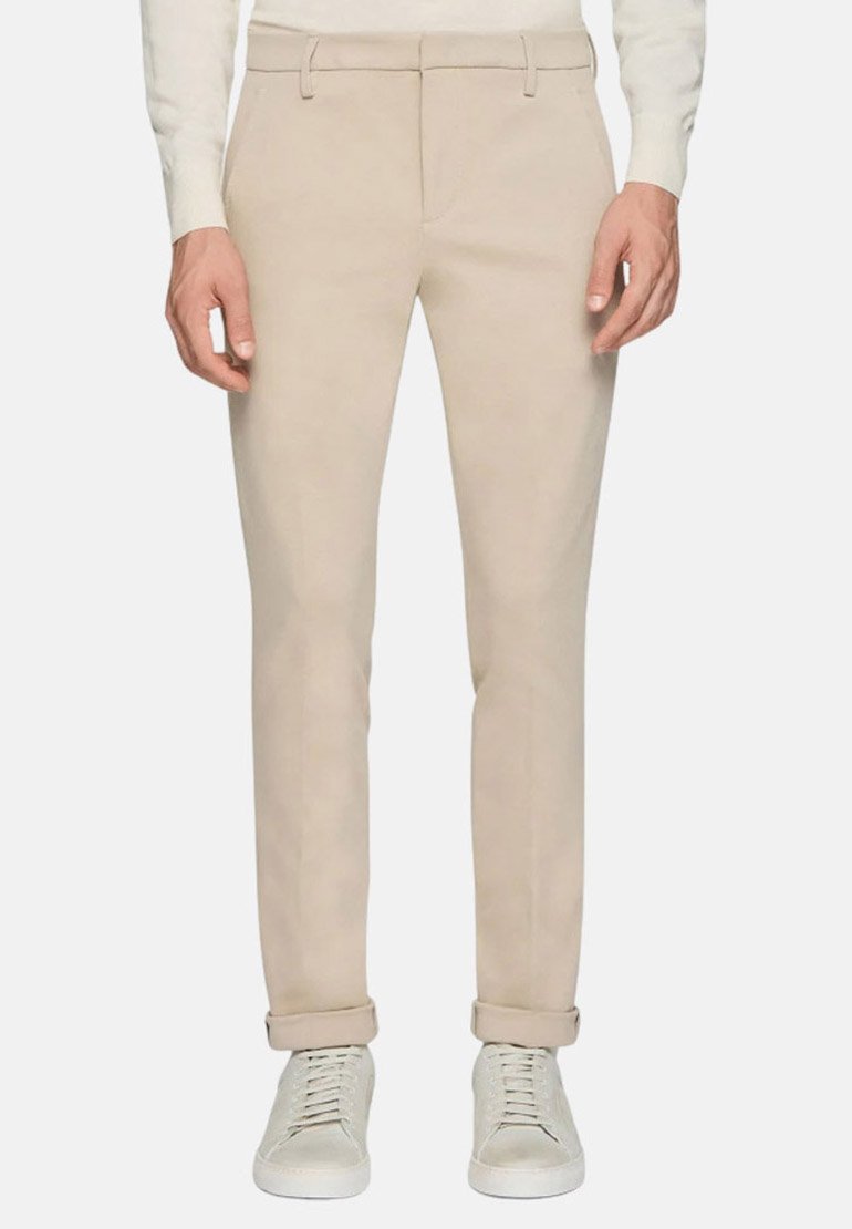 Pantaloni beige su misura realizzati in tessuto liscio, caratterizzati da una vestibilità slim, passanti per la cintura e risvolti, abbinati a sneakers chiare.