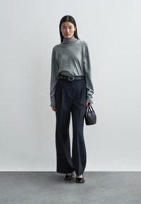 Gray turtleneck sweater, dark high-waisted pleated trousers, black belt, and small black handbag. Sleek texture, minimalistic design.