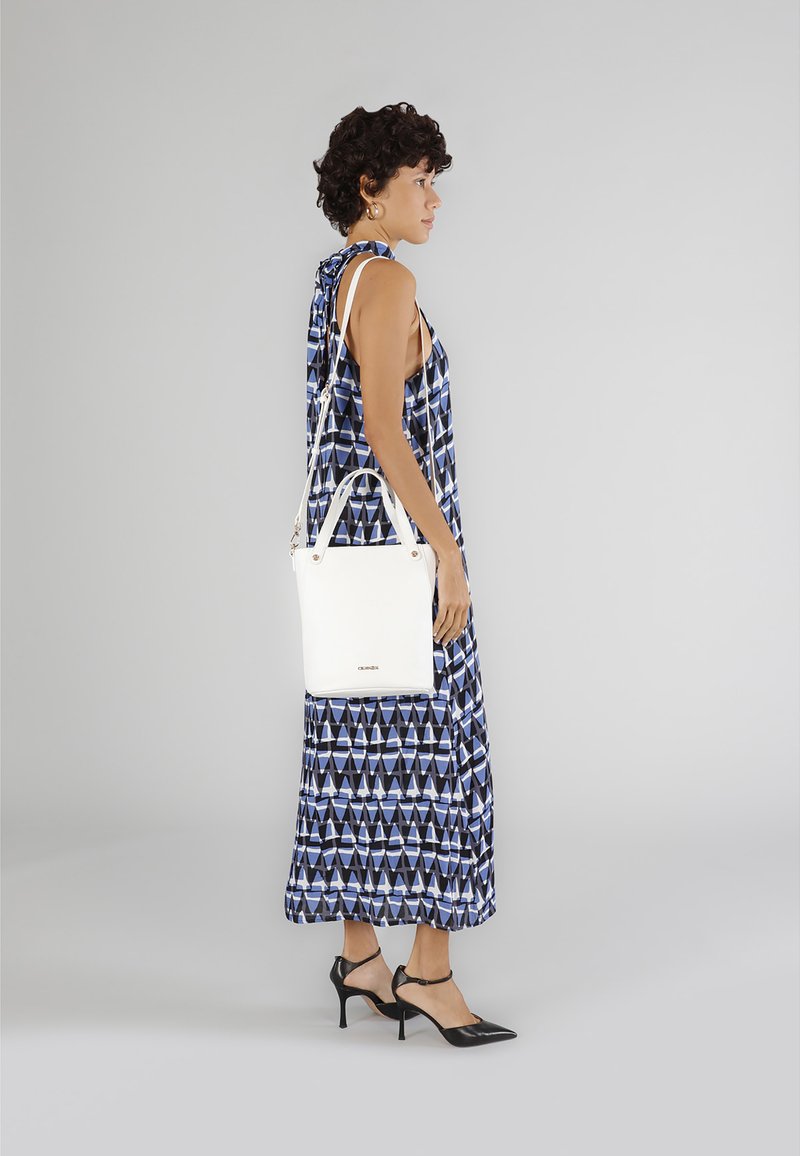 Borsa a tracolla bianca in pelle con design strutturato, indossata da un modello con un maxi dress blu a fantasia geometrica e tacchi neri, vista di profilo.