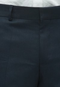 Sötét tengerészkék, testhez szabott nadrág texturált anyagból. Simított derékrésszel és gondosan varrott varratokkal rendelkezik. Minimalista dizájn díszítések nélkül.