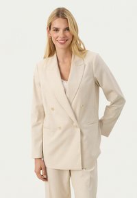 Beige dubbelknäppt kavaj med skräddarsydd passform, slagkrage och två framfickor. Tillverkad av ett smidigt, strukturerat tyg.