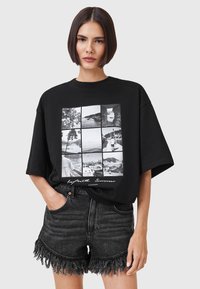 Camiseta negra de gran tamaño con un collage de fotografías en blanco y negro, combinada con pantalones cortos de mezclilla de cintura alta con dobladillos deshilachados.