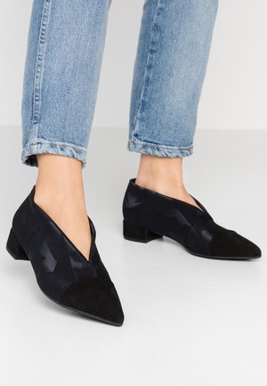 Chaussures noires à talons bas avec un bout pointu. La tige en tissu présente un motif géométrique ; des accents en suède au niveau du bout et du talon apportent un contraste.