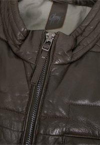 Dunkelbraune Lederjacke mit strukturiertem Finish, ausgestattet mit einem zentralen Reißverschluss und gepolsterten Details an den Schultern. Innenseite in heller Farbe.