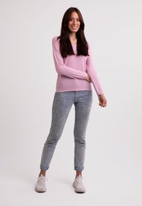 Helles rosa Langarmoberteil kombiniert mit verblassten blauen Skinny-Jeans. Das Outfit hat umgeschlagene Säume und weiße Sportschuhe.