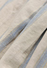 Tela de lino con base beige, con rayas horizontales azules. La textura es ligeramente áspera con un patrón de tejido natural.