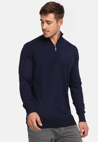 Pull-over en tricot bleu marine à col zippé, en tissu lisse, avec des manches longues et des bords côtelés pour une silhouette ajustée.