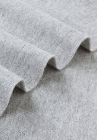 Light gray felt fabric, featuring a soft, textured surface with wavy edges, laid in folds showing its thickness and smooth appearance.