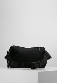 Svart justerbar axelväska i slitstark nylon. Har ett dragkedjefack, mjuk textur och ett brett band med spänne.