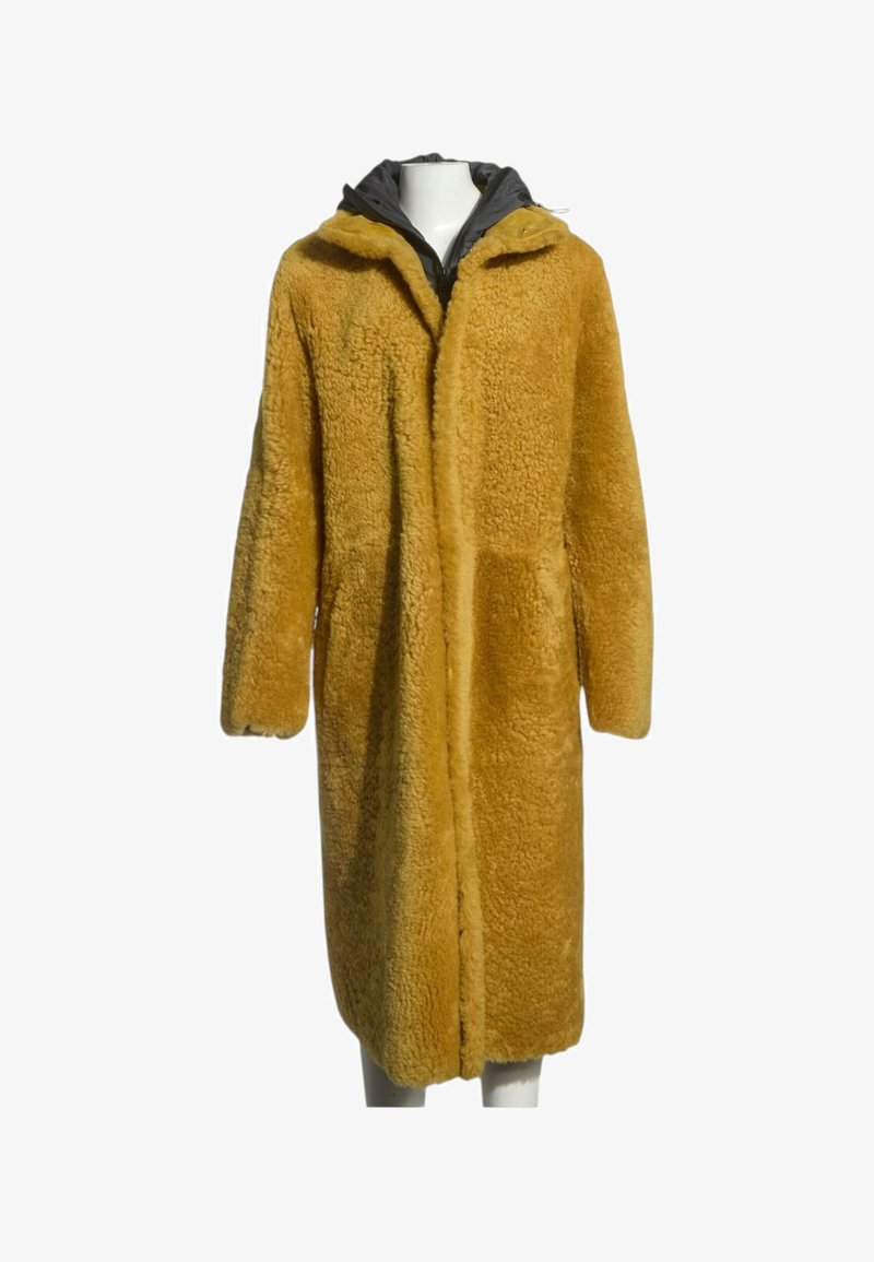 Long manteau en fausse fourrure jaune moutarde avec une capuche noire et des manches longues sur un mannequin blanc.