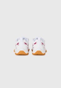 Une paire de chaussures de sport blanches avec des semelles orange et des accents violets, vue de l'arrière sur un fond gris uni.