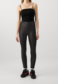 Svarta, figurnära leggings med en slät, glänsande textur. Bärs med en figursydd svart topp och svarta sneakers med röda detaljer.