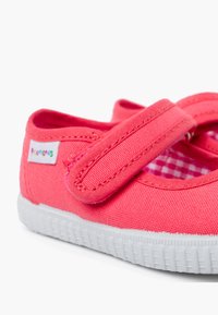 Scarpa in tela rosa con strap in velcro, suola in gomma bianca, fodera a quadri e parte superiore testurizzata. Design leggero e piatto per il massimo comfort.