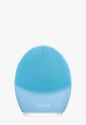 Siliconen gezichtsreiniger, ronde vorm, lichtblauwe kleur, gestructureerd oppervlak met kleine siliconen borsteltjes, doorzichtige basis met "FOREO" branding.